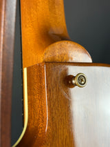 Close-up of a wooden guitar neck with a gold tuning peg against a dark background