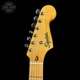 Close-up of the headstock of a Squier Stratocaster electric guitar, showing the maple wood headstock, six silver tuning pegs, and the Squier logo, set against a solid black background.