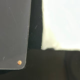 Close-up of a small round copper-colored metal screw or rivet on a black surface, with part of a white object visible at the right edge.