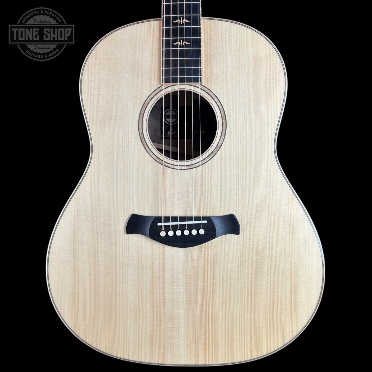 An acoustic guitar with a natural wood finish and black hardware, shown against a solid black background with a Tone Shop logo in the top-left corner.
