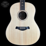 An acoustic guitar with a natural wood finish and black hardware, shown against a solid black background with a Tone Shop logo in the top-left corner.