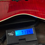 A close-up of a red wood-grain instrument body resting on a black digital scale with a blue display reading 7.134 kg.