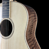 Close-up of an acoustic guitar body showing the natural wood grain top, sound hole rosette, and dark fingerboard against a black background.