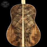 The back of an acoustic guitar made of richly figured wood, showing a prominent maple center stripe and swirling grain patterns in brown and beige tones, set against a solid black background.