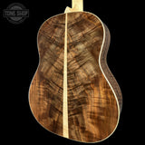 The back of an acoustic guitar made from richly figured brown wood, featuring a central light wood strip and a white binding, shown against a solid black background with a Tone Shop watermark in the top left.