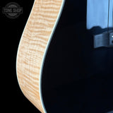 Close-up of a guitar with a black finish and wooden neck, branded 'Tone Shop'.
