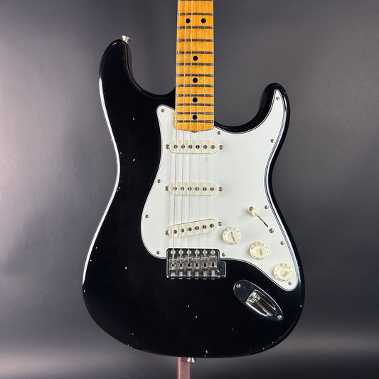 Black electric guitar with a wooden fretboard on a gray background