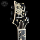 Close-up of a guitar headstock and upper neck against a black background, featuring a black glossy finish with gold-toned hardware, bird inlays on the headstock, and bird inlays on the fretboard. A Tone Shop watermark is visible in the top left corner.