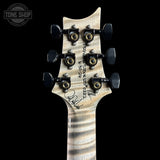 Close-up of the headstock of a custom electric guitar against a solid black background. The headstock features a light-colored flamed maple top with a black signature, serial number 'P1-2025-370-28', and gold-toned tuning pegs.