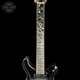 Close-up of an electric guitar neck and lower body against a black background, featuring a glossy black flamed maple finish, gold fretboard binding, and bird inlays on the fretboard. A Tone Shop watermark is visible in the top-left corner.