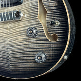 Close-up of a semi-hollow electric guitar body showing the flamed maple top, f-hole cutout, chrome hardware, and control knobs against a black background.
