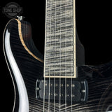 Close-up of an electric guitar body and neck showing a glossy black flamed maple finish, black humbucker pickups, and a light wood fretboard against a black background.