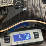 Close-up of an electric guitar body resting on a digital kitchen scale displaying its weight in ounces and pounds.