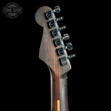 Close-up of the headstock of a Marshall electric guitar, showing the dark brown wood grain and six black tuning pegs with Marshall logos, set against a solid black background.