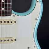 Close-up of an electric guitar body showing a light blue body contour, cream pickguard, cream humbucker pickups, and part of the dark fretboard against a black background.