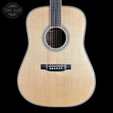 A front-facing acoustic guitar with a natural wood finish and black hardware, shown against a solid black background with a Tone Shop watermark in the top-left corner.