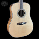 An acoustic guitar with a natural wood finish and a black bridge, shown against a solid black background with a Tone Shop watermark in the top-left corner.