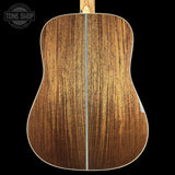The back of an acoustic guitar made of rich brown wood with a natural grain pattern, shown against a solid black background with a Tone Shop logo in the top left corner.