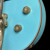 Close-up of a turquoise guitar with gold hardware on a black background