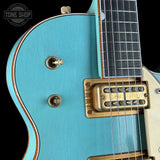 Close-up of a turquoise electric guitar with a gold pickup and control knobs, featuring 'Tone Shop' branding.