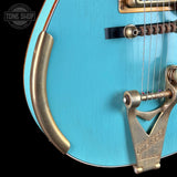 Close-up of a blue resonator guitar with a Gibson brand label on a black background.