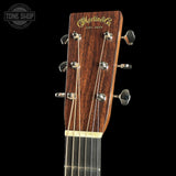 Close-up of the headstock of a Martin & Co. acoustic guitar against a solid black background, showing the dark wood grain and silver tuning pegs.