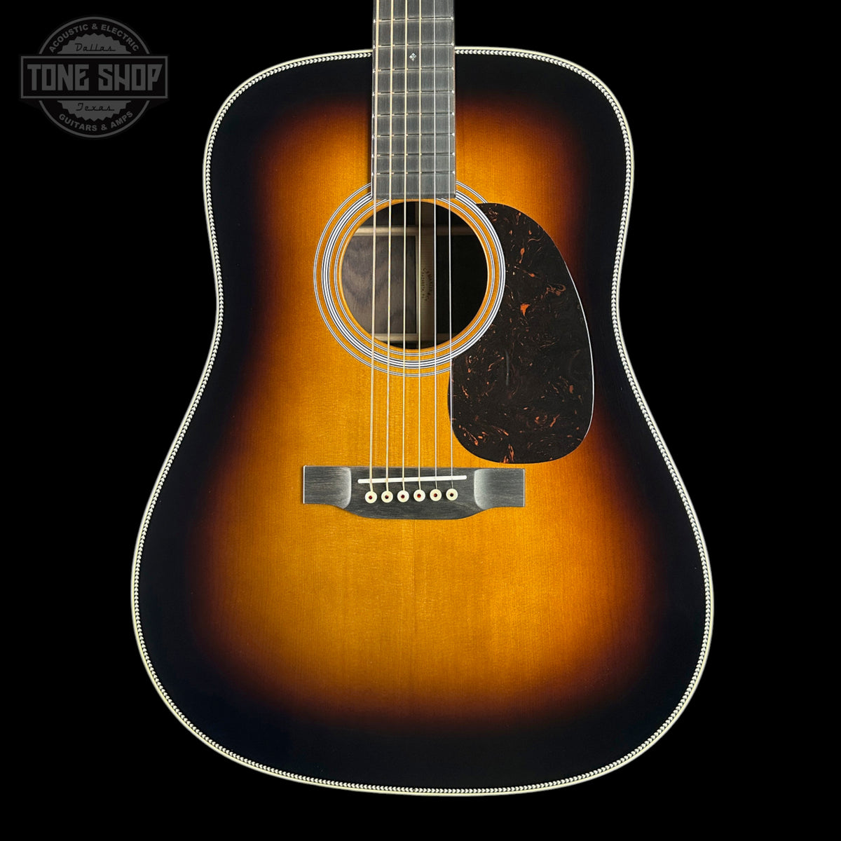 A classic acoustic guitar with a sunburst finish, featuring a warm amber center fading to a dark black edge, set against a solid black background with a Tone Shop logo in the top-left corner.