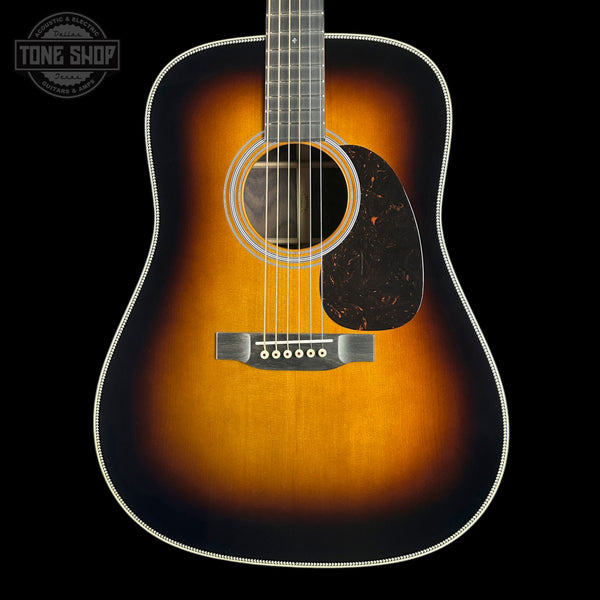 A classic acoustic guitar with a sunburst finish, featuring a warm amber center fading to a dark black edge, set against a solid black background with a Tone Shop logo in the top-left corner.