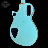 Back view of a turquoise electric guitar with 'Tone Shop' logo.