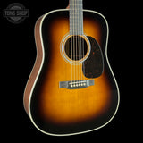 A classic acoustic guitar with a sunburst finish, featuring a warm amber center fading to a dark black edge, set against a solid black background with a Tone Shop logo in the top-left corner.