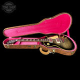 An electric guitar with a black flame-grain finish resting inside an open hard case with a bright pink velvet interior. The guitar features gold hardware and a cream pickguard.