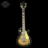 A Gibson electric guitar with a natural flame maple top, shown against a solid black background. The guitar features a dark brown fretboard, gold hardware, and a white pickguard.