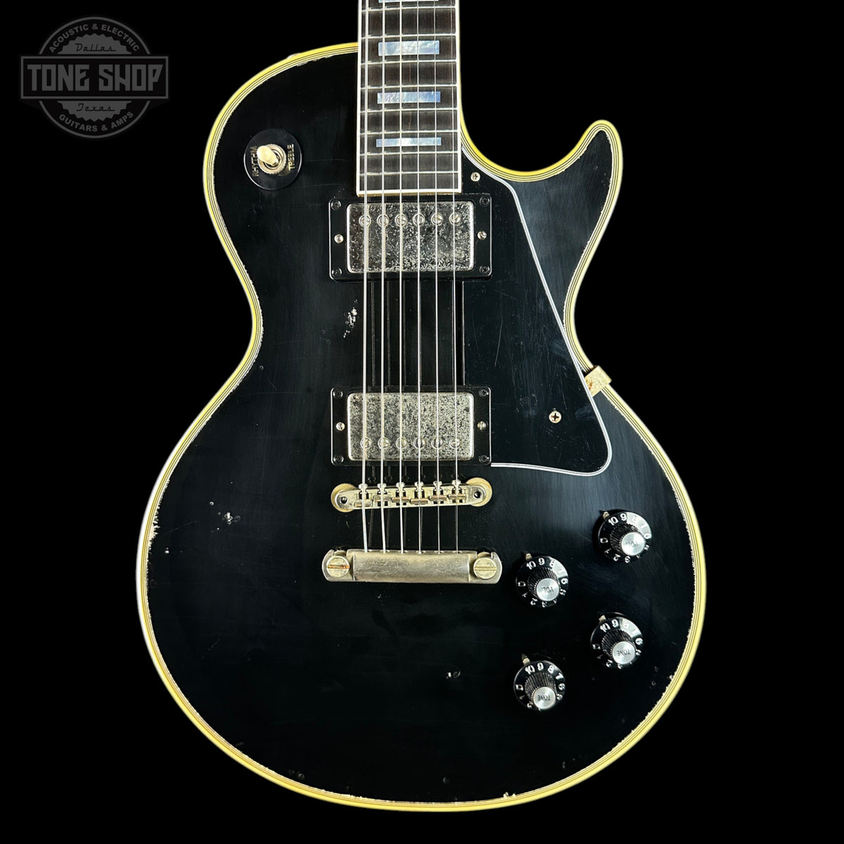 A black electric guitar with gold trim and hardware, photographed against a solid black background. A circular 'TONE SHOP' watermark is visible in the top-left corner.