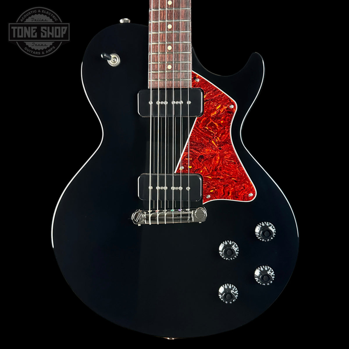 A black electric guitar with a red maple pickguard and a dark wood fretboard, shown against a solid black background. A Tone Shop watermark is visible in the top-left corner.