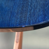 Close-up of a blue textured fabric or material surface with a curved edge and a small metallic fastener, with a blurred copper-toned support visible below.