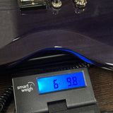 A close-up of a guitar body resting on a digital smart weigh scale, showing the scale's blue display screen reading 6 lbs 9.8 oz.
