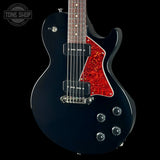 A black electric guitar with a red glitter-style pickguard, shown against a black background with a Tone Shop watermark in the top-left corner.