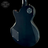 The rear view of a black electric guitar against a solid black background, showing the back body, pickups, and tailpiece. A Tone Shop watermark is visible in the top-left corner.
