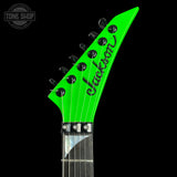 Close-up of the headstock of a Jackson electric guitar in bright neon green, showing the brand name in black script and tuning pegs, set against a solid black background.