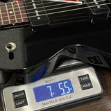 A close-up of a black electric guitar body resting on a digital scale, showing the scale display reading 7.55 lbs and the guitar's glossy finish and control buttons.
