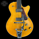 A close-up of a yellow-orange electric guitar body with a dark brown pickguard, chrome hardware, and a silver Leslie speaker mount against a black background. A Tone Shop watermark is visible in the top left corner.