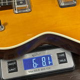A close-up of a guitar body resting on a digital scale, showing the scale reading 6.81 lbs.