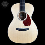 Front view of an acoustic guitar with a natural wood finish and a dark red pickguard, shown against a solid black background with a Tone Shop watermark in the top left corner.