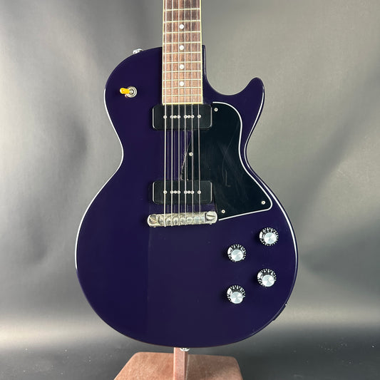 Purple electric guitar on a stand against a gray background