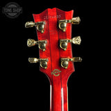 Close-up of the headstock of a red electric guitar against a black background, showing six gold tuning pegs and a gold-toned logo on the back.