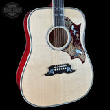 A close-up studio shot of a Taylor acoustic guitar against a solid black background, featuring a natural wood top, red sides, and intricate bird inlays on the pickguard and upper bout.
