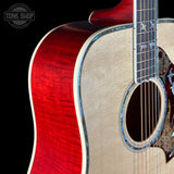 Close-up of an acoustic guitar body showing a bright red flamed maple top, natural wood soundboard, and decorative inlay around the sound hole, photographed against a black background with a Tone Shop watermark.