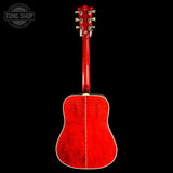 A red acoustic guitar shown from the back, featuring a glossy cherry-red finish and gold tuning keys, set against a solid black background with a Tone Shop watermark in the top-left corner.