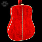 The back of an acoustic guitar with a vibrant red flamed maple wood finish, featuring a cream-colored neck joint and binding, shown against a solid black background.