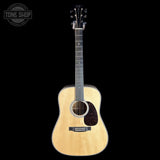 A natural wood acoustic guitar with a dark pickguard and headstock, shown against a solid black background. A 'TONE SHOP' watermark is visible in the top-left corner.